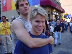 two young men standing next to each other in front of a group of people on the street