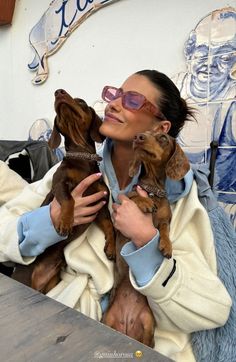 a woman holding two small dogs while sitting at a table