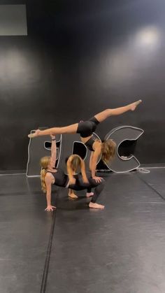 three young women doing acrobatic on the floor in front of a sign