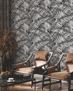 two chairs and a table in front of a wall with black and white leaves on it