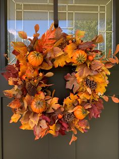 a wreath with leaves and pine cones hanging from the front door, decorated with autumn foliage