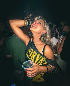 a woman drinking from a cup while standing in front of a crowd at a concert