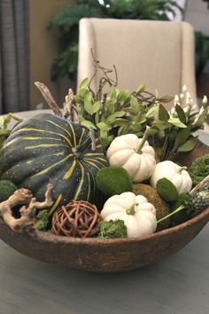 a bowl filled with white and green pumpkins on top of a table next to a chair