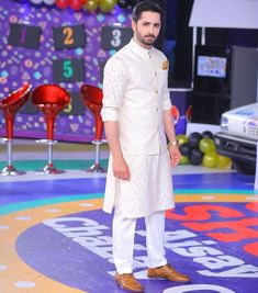 a man in a white outfit standing on a colorful stage with balloons and decorations behind him