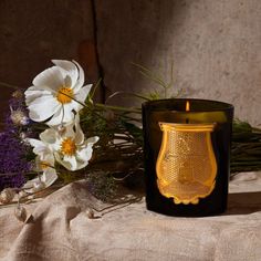 a candle and some flowers are on a table with a brown cloth in front of it