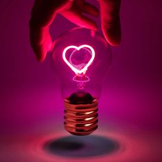 a hand holding a light bulb with a heart shaped light on it's side