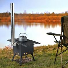 an outdoor stove next to a camping chair on the grass near a body of water