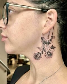 a woman's neck with a flower tattoo on her left side and behind the ear