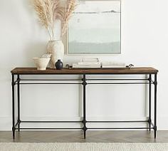 a table with some plants on it in front of a white wall and a painting