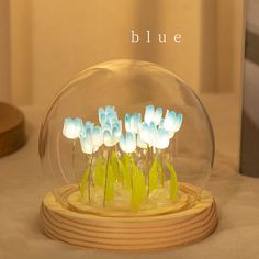 blue flowers in a glass bowl on a wooden stand with the word blue above it