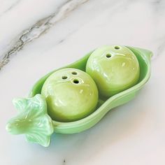 two peas in a pea pod shaped dish on a marble countertop, with the tops painted green