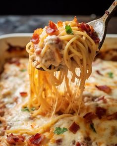 a spoon full of spaghetti with meat and cheese on it is being lifted from a casserole dish