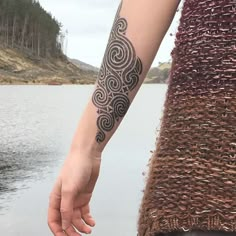 a woman with a tattoo on her arm holding the hand of another person near a body of water