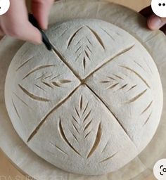 a person is carving an intricate design on a round piece of bread that they are holding in their hands