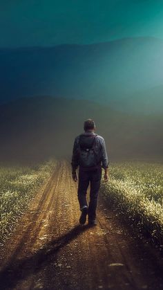 a man walking down a dirt road towards the sun