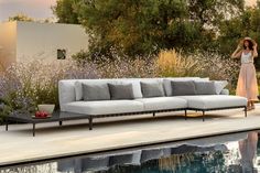 a woman standing next to a couch near a swimming pool with flowers in the background