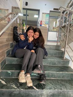 two young women sitting on the steps in front of some stairs and smiling at the camera