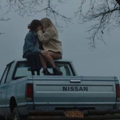 two people are sitting on the back of a pickup truck, one is kissing the other