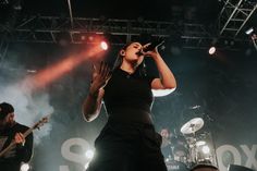 a woman standing on top of a stage holding her hands up in the air while singing