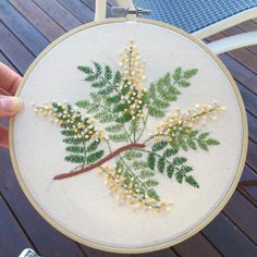 a person holding up a small embroidered plant with yellow flowers and green leaves on it