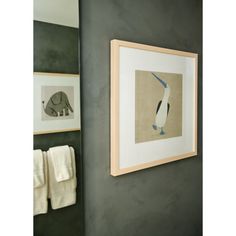 a bathroom with two towels hanging on the wall and an elephant framed in wood frame