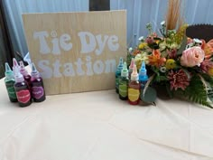 there are some bottles on the table with flowers next to it and a sign that says tie dye station