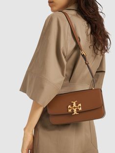 Height: 12.5cm Width: 23.5cm Depth: 6.2cm. Leather strap. Front flap with magnetic closure. Front metal logo detail. One internal zip pocket Tory Burch Eleanor Bag, Tory Burch Shoulder Bag, Tory Burch Bag, Purple Bags, Brown Bags, Metal Logo, Metallic Logo, Women's Bags, Magnetic Closure