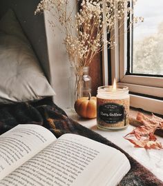 an open book sitting on top of a table next to a candle and some flowers