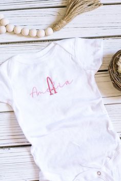 This beautifully custom embroidered 0-to-3 month short-sleeved baby bodysuit makes the perfect outfit for your new little baby girl! This comfortable and soft baby bodysuit with snaps features high quality embroidery thread that upgrades a baby one-piece! Personalized with your baby girl's name and monogram initial in beautiful script font, this summer baby clothing is a great way to celebrate your newborn's arrival. A meaningful custom baby gift new parents will love. This listing is for a custom 0-3 MONTH sized short-sleeve baby bodysuit. Buyer customization options are:  * choice of bodysuit color (oat, white) * choice of first initial and baby name  * choice of embroidery thread color (see swatch chart in listing photos) Please allow 1-3 business days processing time from date of order Personalized Fitted White Bodysuit, White Personalized Short Sleeve Onesie, Cotton Onesie For Baptism, White Short Sleeve Onesie For First Birthday, Cotton Baptism Onesie With Short Sleeves, Personalized Fitted Short Sleeve Onesie, White Short Sleeve Onesie For Baptism, Fitted White Onesie For Baptism, Personalized Fitted Short Sleeve Bodysuit