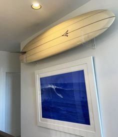 a white surfboard hanging on the wall above a blue ocean painting and framed photograph