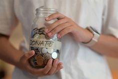 a person holding a jar full of coins with the word donation taped to it's side