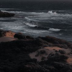 an ocean view with waves crashing on the shore and dark clouds in the sky above