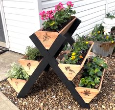 three wooden planters with flowers in them on the side of a house next to gravel