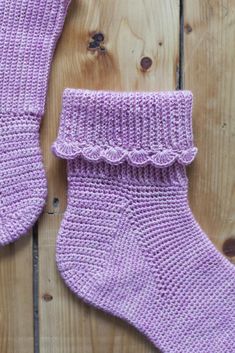 a pair of purple knitted socks sitting on top of a wooden floor next to a piece of wood