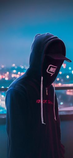 a person wearing a hoodie looking out over a city at night with lights in the background