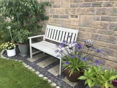 a white bench sitting next to a brick wall with potted plants on top of it