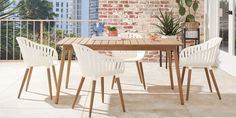 a wooden table with white chairs on top of it next to a brick wall and potted plant