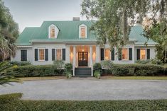 a white house with green roof and black shutters on the front door, surrounded by trees