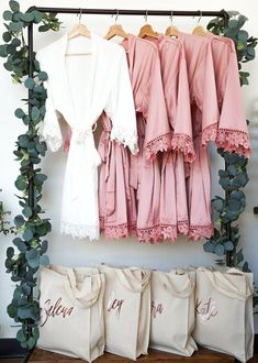 pink and white robes hanging on a rack with personalized tote bags next to them