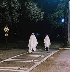 two people dressed in white walking down the street at night with ghost costumes on their heads