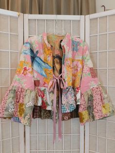 a colorful jacket hanging on the side of a white wall next to a window with sheer curtains