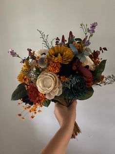 a hand holding a bouquet of flowers on a white background with oranges, yellows and purples