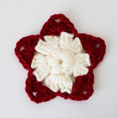 a crocheted red and white flower on a white surface