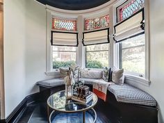 a living room filled with furniture next to two large windows and a round table in front of the window