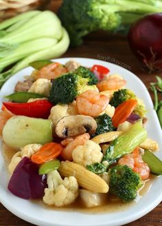 a white plate topped with shrimp, broccoli and cauliflower next to celery