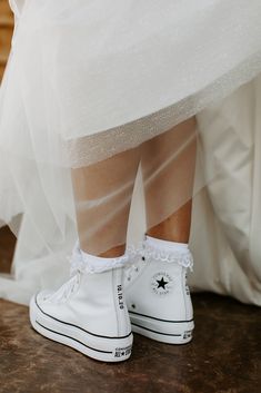 a person wearing white converse shoes standing on top of a wooden floor next to a wedding dress