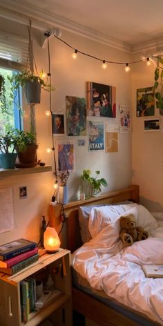 an unmade bed in a small room with lights strung from the ceiling and posters on the wall