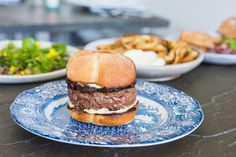 a hamburger sitting on top of a blue and white plate next to bowls of food