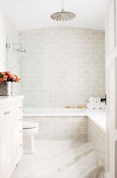 a white bathroom with a tub, toilet and flowers in the vase on the counter