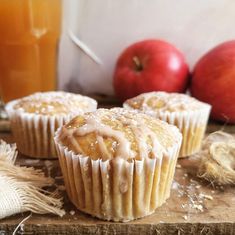 three muffins sitting on top of a wooden cutting board next to an apple